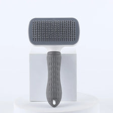 A gray pet hair removal brush with massage pins is displayed on a white stand.