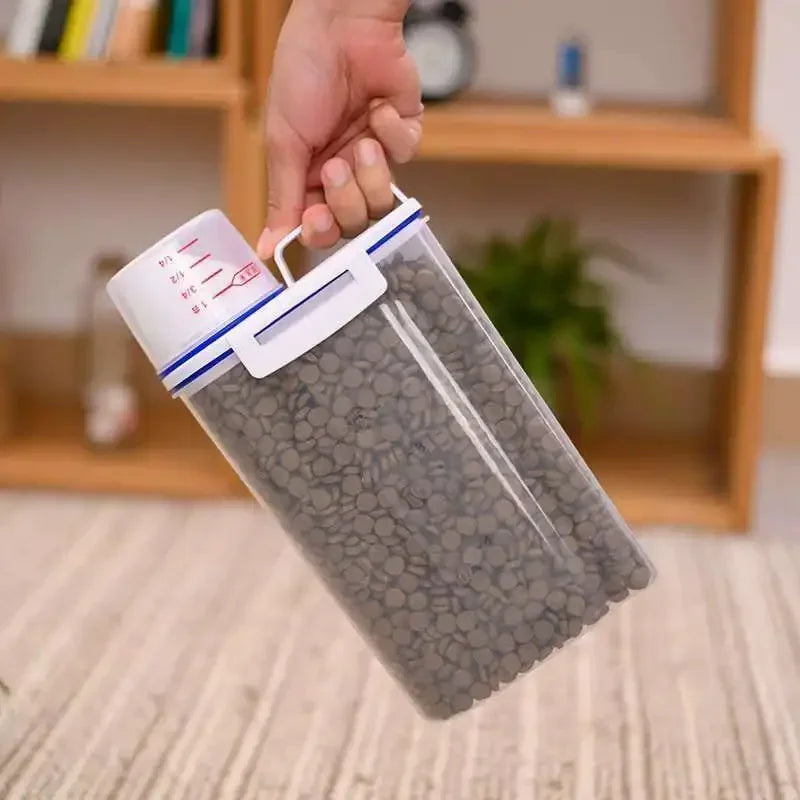 A hand is holding an airtight pet food storage container with a measuring cup, filled with gray pellets.