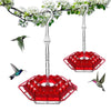 A hanging hummingbird feeder with a red, hexagonal bowl and clear glass tubing, suspended from a leafy branch.