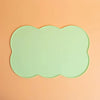 A light mint green silicone pet feeding mat with a scalloped edge resting on a peach-colored surface.