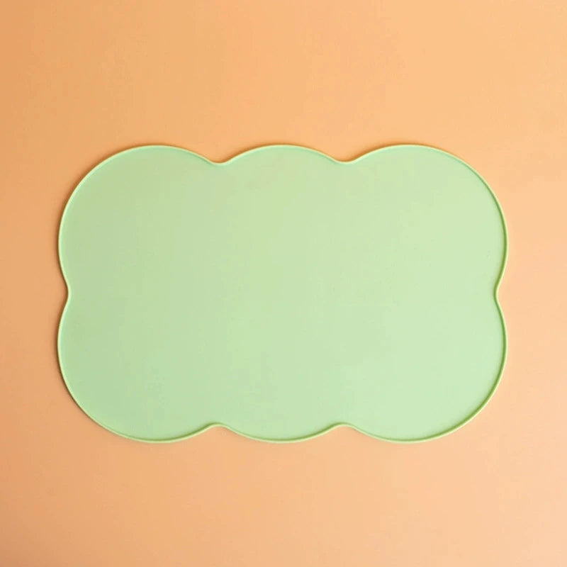 A light mint green silicone pet feeding mat with a scalloped edge resting on a peach-colored surface.