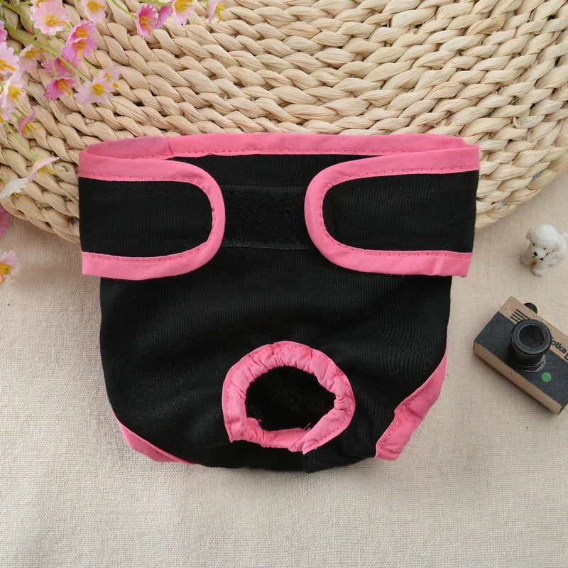 A black reusable dog diaper with pink trim is displayed on a woven mat.