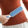 A hand holds a blue lint remover brush against a brown sweater, demonstrating its use for removing pet hair and lint.