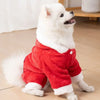 Un perro blanco y esponjoso con un mono peludo rojo sentado en un suelo de madera.