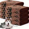 A stack of brown pet bath towels with paw print designs, next to a small dog.