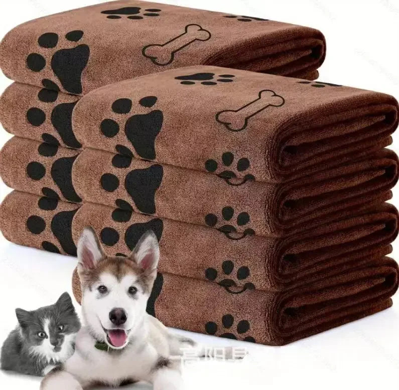 A stack of brown pet bath towels with paw print designs, next to a small dog.