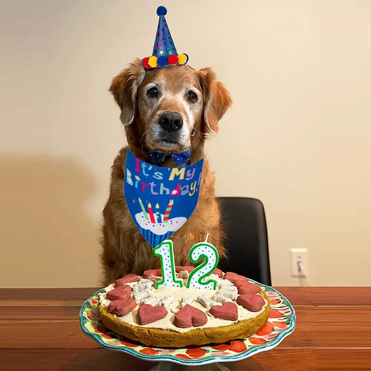 A golden retriever wearing a party hat and a blue birthday banner sits behind a cake.