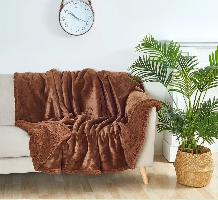 A brown velvet blanket draped over a light-colored sofa next to a potted palm plant.