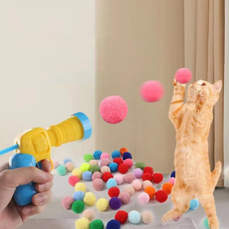 Eine Hand hält eine gelbe Spielzeugwaffe, die rosa und grüne Plüschbälle auf eine orange Katze feuert.