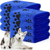 A stack of blue pet bath towels with black paw prints, next to a white dog.