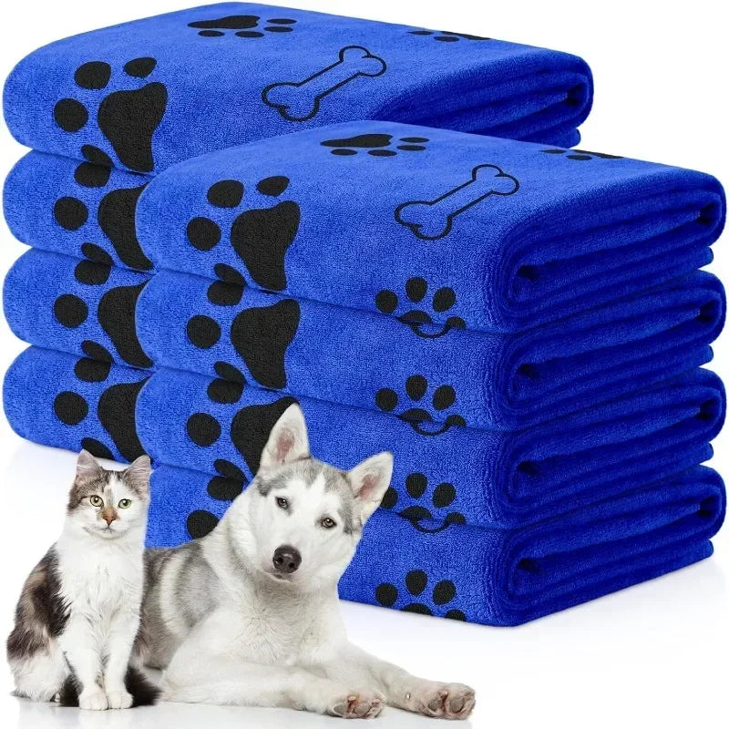 A stack of blue pet bath towels with black paw prints, next to a white dog.