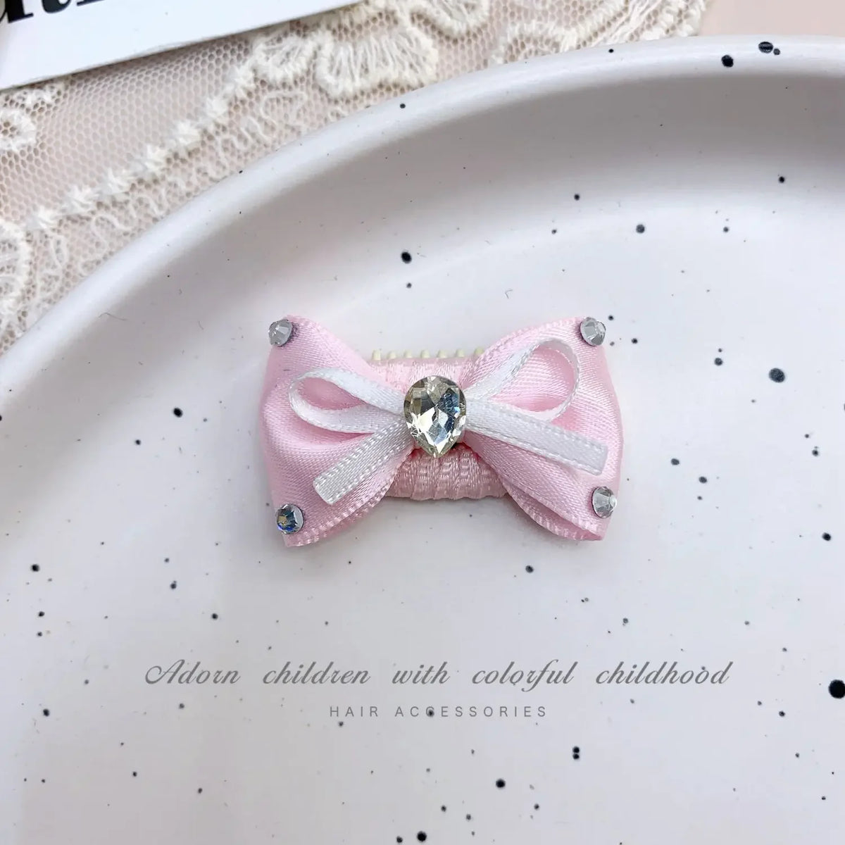 Pink bow hair accessory with rhinestone pearl accents displayed on a white plate.