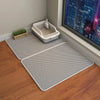 Un tapis anti-eau gris pour litière de chat est posé sur un plancher en bois à côté d'une boîte pour chat blanche et d'une vu