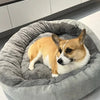 Ein hellbraunes und weißes Shiba Inu-Hund ruht in einem grauen, flauschigen Hundebett.