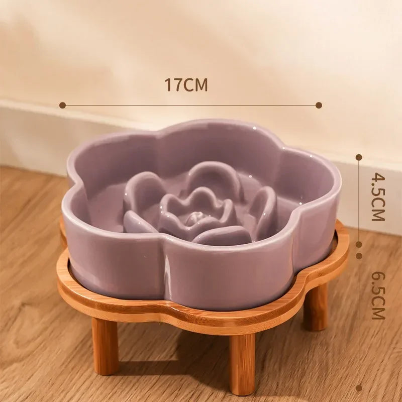 A purple ceramic slow feeder cat bowl rests on a natural wooden stand.