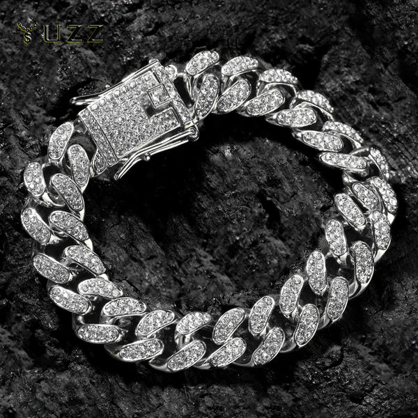 A silver Cuban link chain bracelet adorned with clear rhinestones, photographed against a dark, textured background.