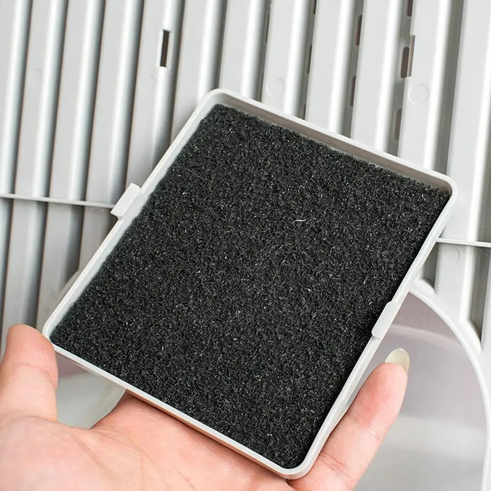 A hand holds a rectangular black activated carbon filter pad for cat litter boxes against a white plastic frame.