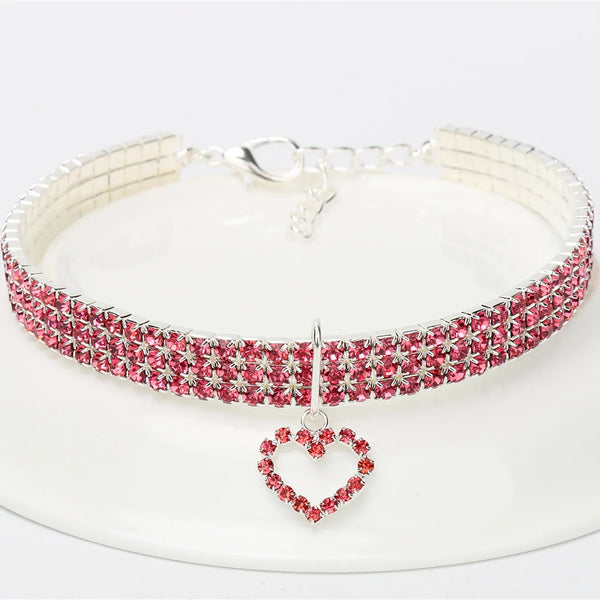A sparkling rhinestone pet collar necklace with a pink and silver band displayed on a white plate.