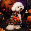 A white poodle wearing a black and orange Halloween princess dress with an orange bow, set against a spooky backdrop.