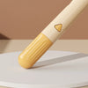A light yellow self-cleaning pet brush with massage pins resting on a beige surface.