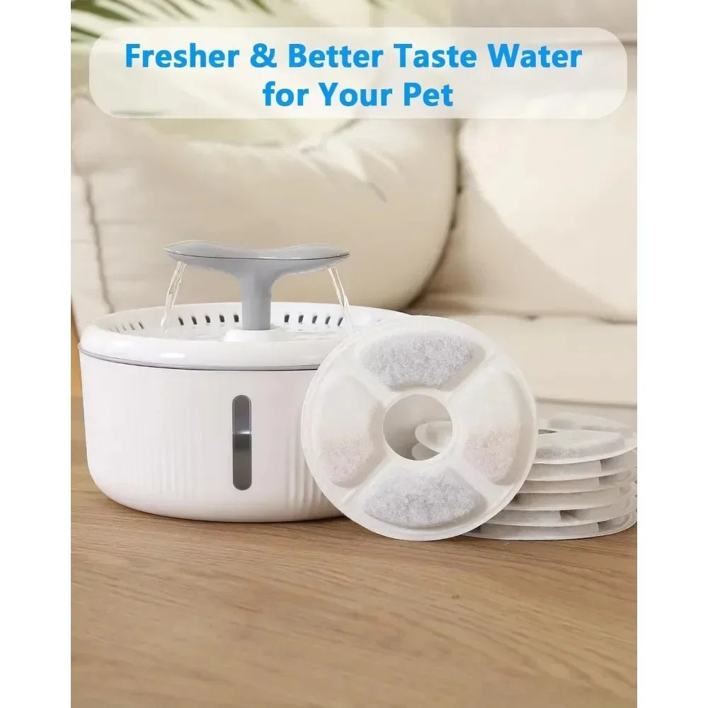 A white water fountain with a gray spout and replacement activated carbon filters is shown on a wooden surface.