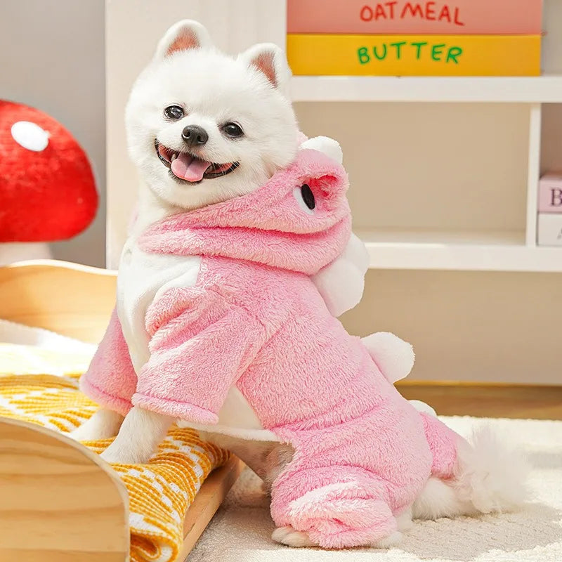 A white dog wearing a pink fleece hoodie with animal ears sitting on a light-colored rug.