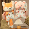 A hand holds a pink and orange cartoon animal bean bag plush toy featuring a pig and a fox.