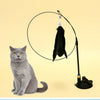 A gray cat sits next to a black suction cup wand with a feather toy attached, demonstrating the cat teaser.
