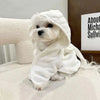 A white dog wearing a fluffy white multi-purpose pet bath robe, looking directly at the camera.