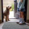 Una niña con suéter azul claro y falda de mezclilla está junto a un perro en un umbral con una alfombra gris.