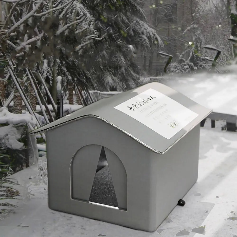 A gray foldable waterproof insulated cat house with a triangular window sits in a snowy outdoor setting.
