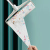A hand holds an extendable pet hair lint roller with a patterned white and pink lint roll against a teal background.