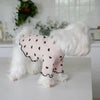 Ein weißer flauschiger Hund trägt eine rosa Weste mit schwarzen Herzen auf der Brust.