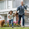 A family of four is running outdoors with a dog in a sunny, residential setting.