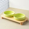 A bright lime green ceramic cat and dog bowl rests on a wooden stand next to a window.