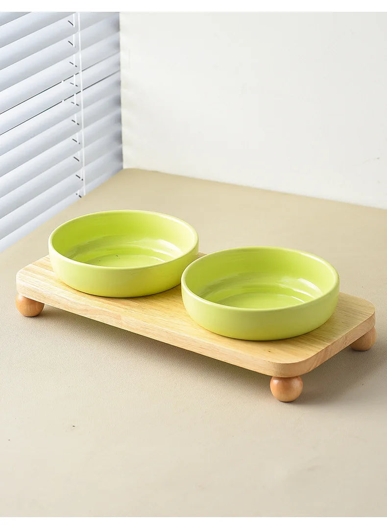 A bright lime green ceramic cat and dog bowl rests on a wooden stand next to a window.
