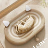 A light beige sisal board with concentric grooves features a small cream-colored cat lying on it, accompanied by white chew t