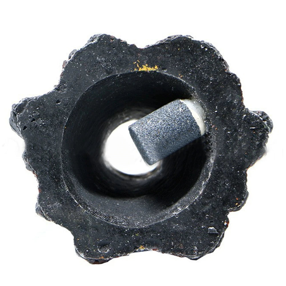 A black, porous stone with a central opening and a cylindrical piece inserted into it.