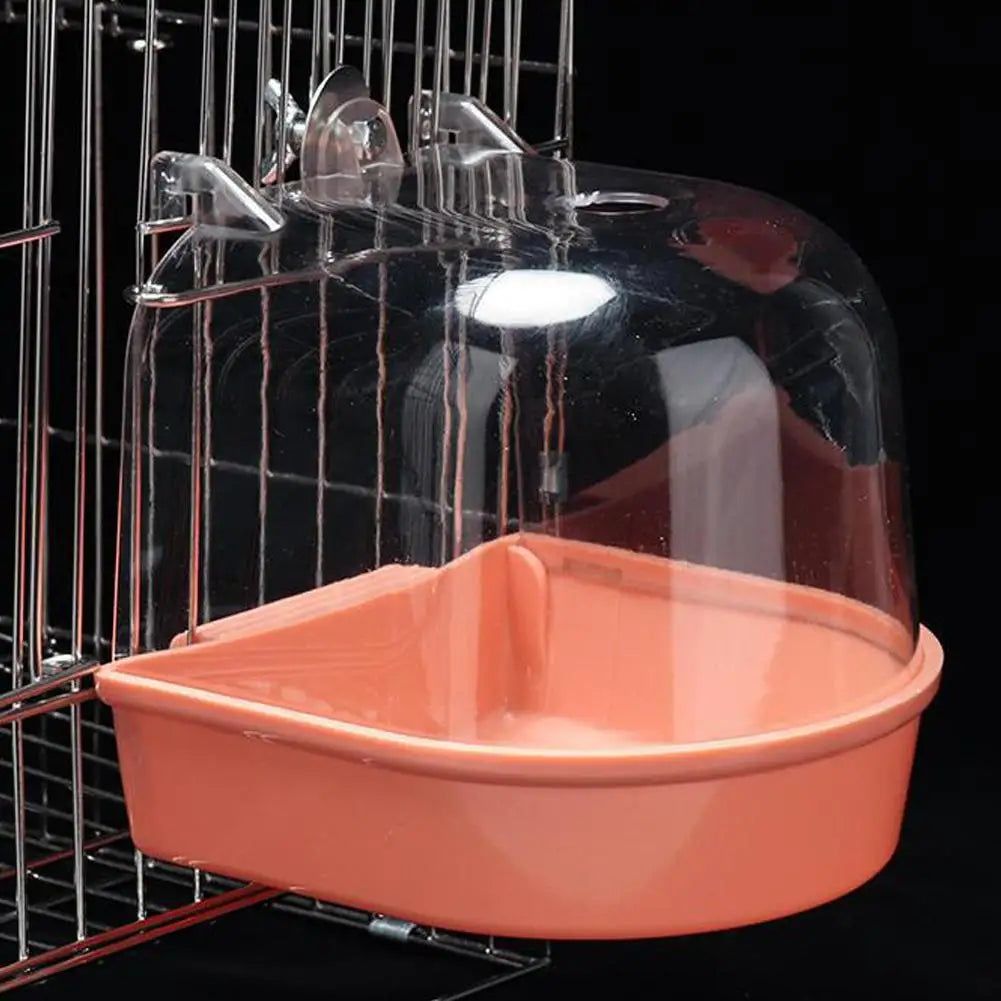 A clear plastic hanging bird bath with an orange base is suspended in a wire cage.
