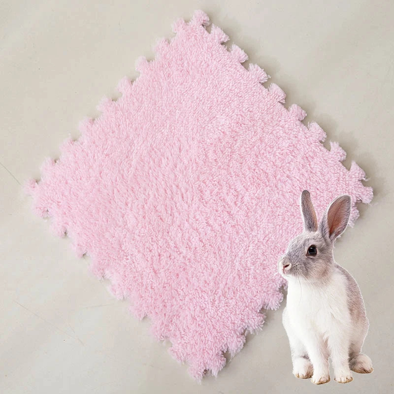 A small gray rabbit sits on a pink, fluffy fleece pet warming mat.