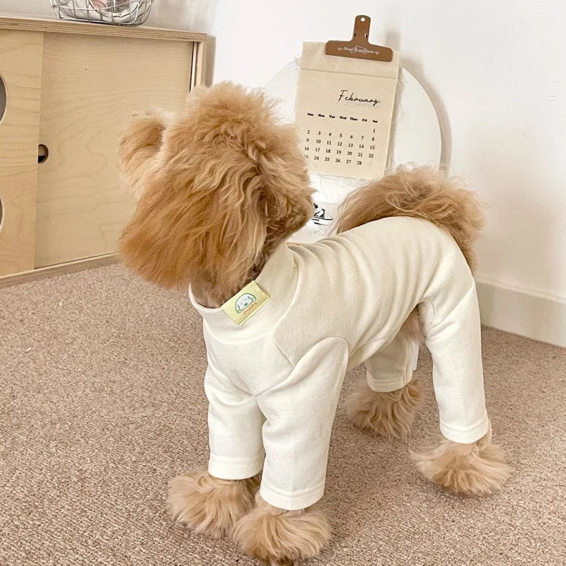 A light beige soft stretch dog pajama jumpsuit for a small to medium pet standing on a carpet.