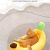 A fluffy orange cat is relaxing in a yellow, banana-shaped plush pet bed.