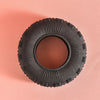 A close-up view of a black rubber chew toy with deep treads resting on a light pink surface.