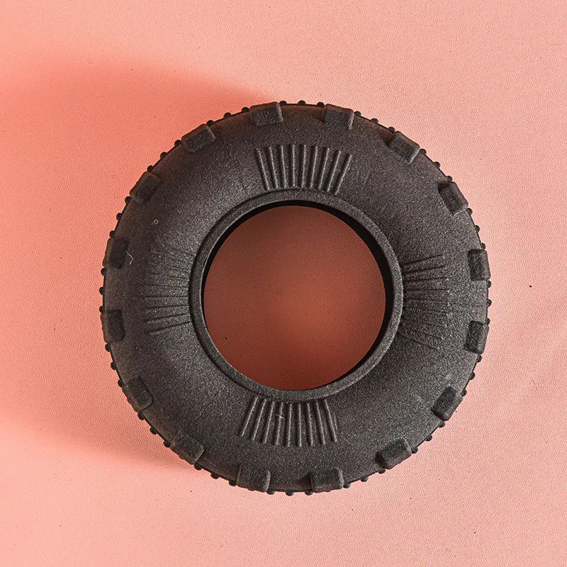 A close-up view of a black rubber chew toy with deep treads resting on a light pink surface.
