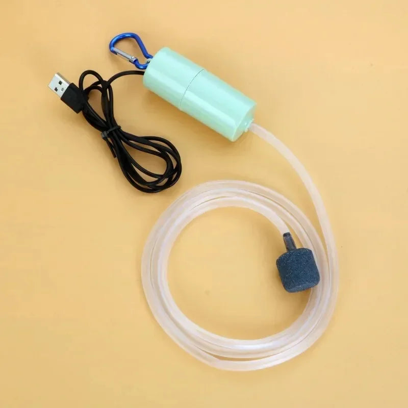 A portable USB aquarium air pump with a blue clip and clear tubing is shown on a light brown surface.