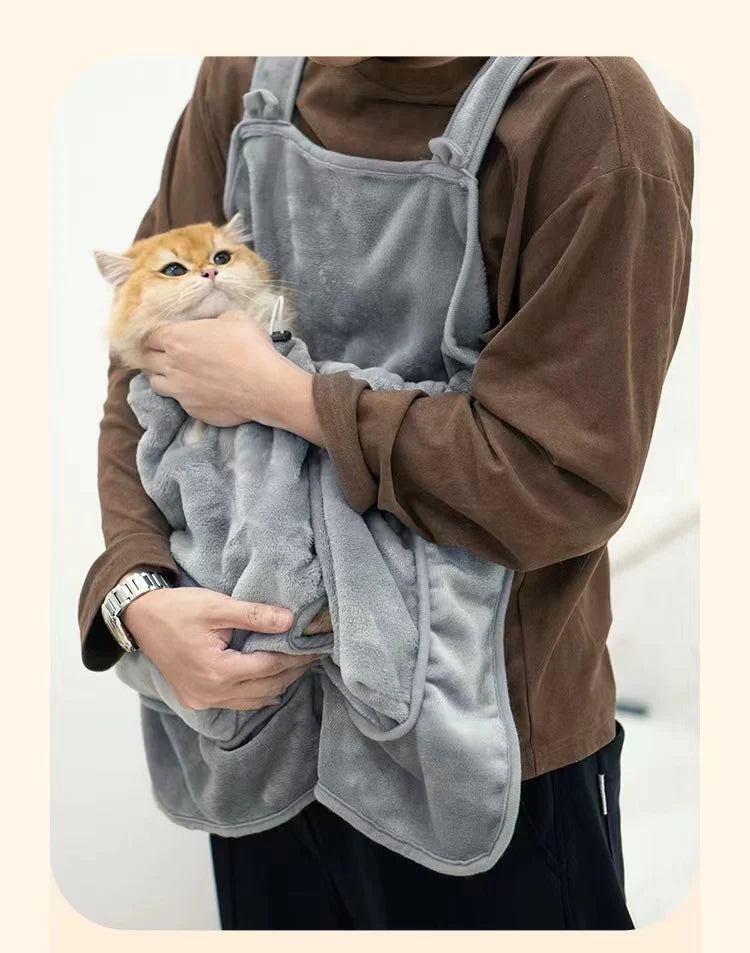 Una persona lleva un delantal para mascotas gris al aire libre mientras sostiene un pequeño gato naranja.