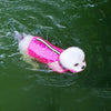 A white dog wearing a pink life jacket swims in green water.