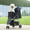 A black 3-wheel foldable pet stroller with a white poodle sits on a paved surface.