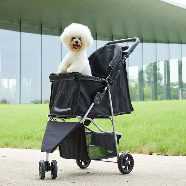 A black 3-wheel foldable pet stroller with a white poodle sits on a paved surface.