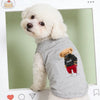 A fluffy white dog wearing a gray printed vest with a brown bear graphic.